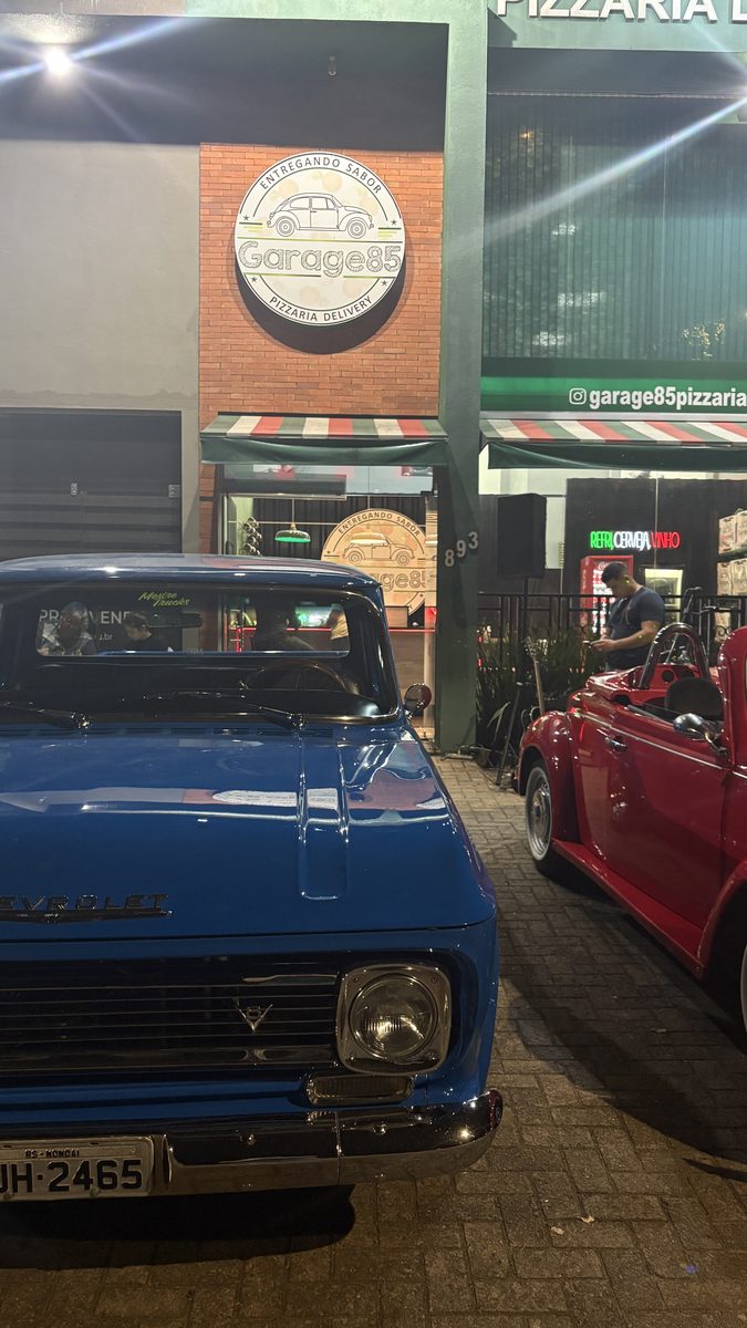 Caminhonete azul e Fusca conversível vermelho embaixo do crest da Garage85