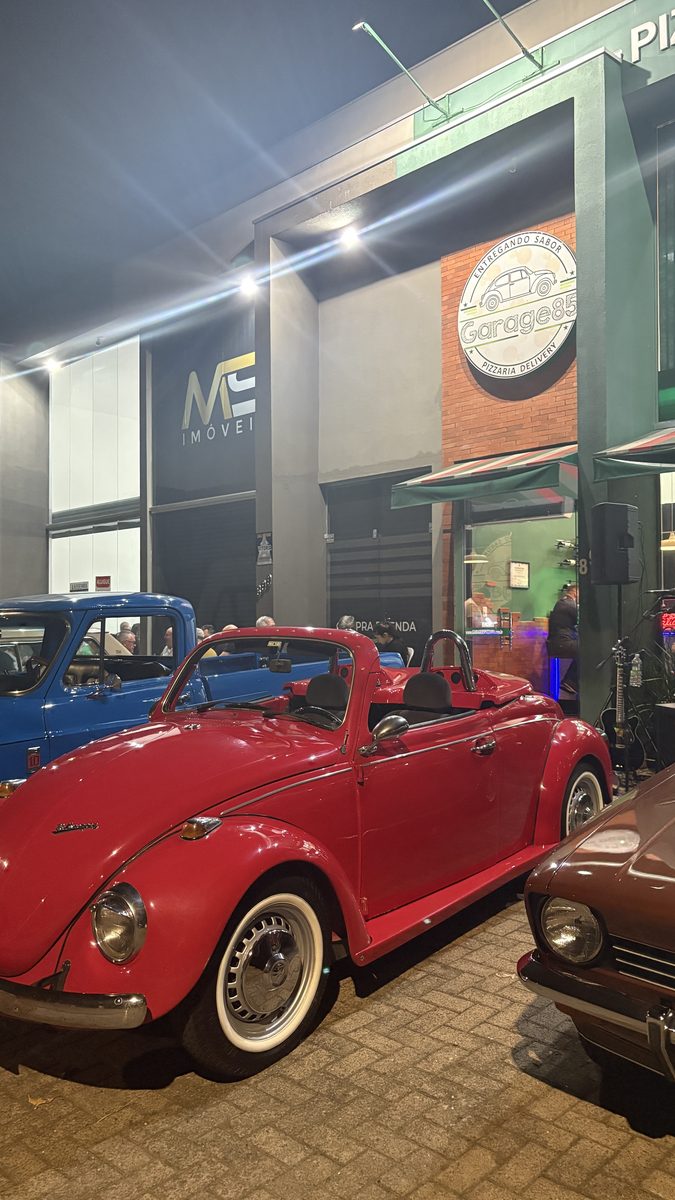 Fusca conversível vermelho na frente da fachada da Garage85 à noite