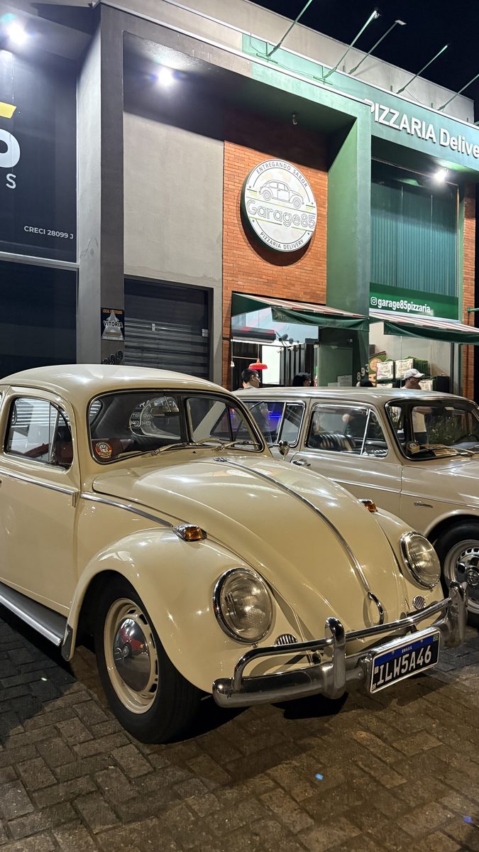 Fusca creme de perto, com o crest da Garage85 ao fundo