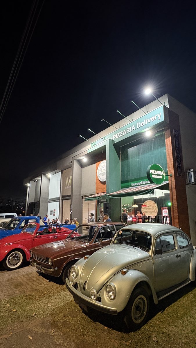 Carros clássicos alinhados com a fachada da Garage85 iluminada