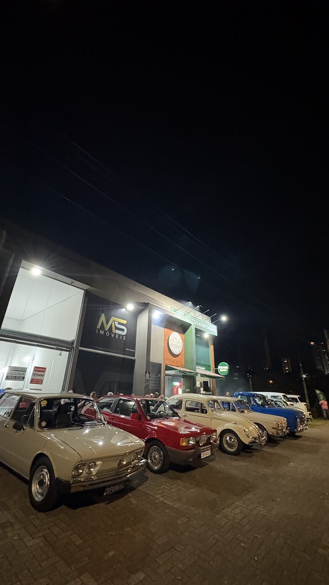 Vista ampla da fila de carros antigos na frente da pizzaria