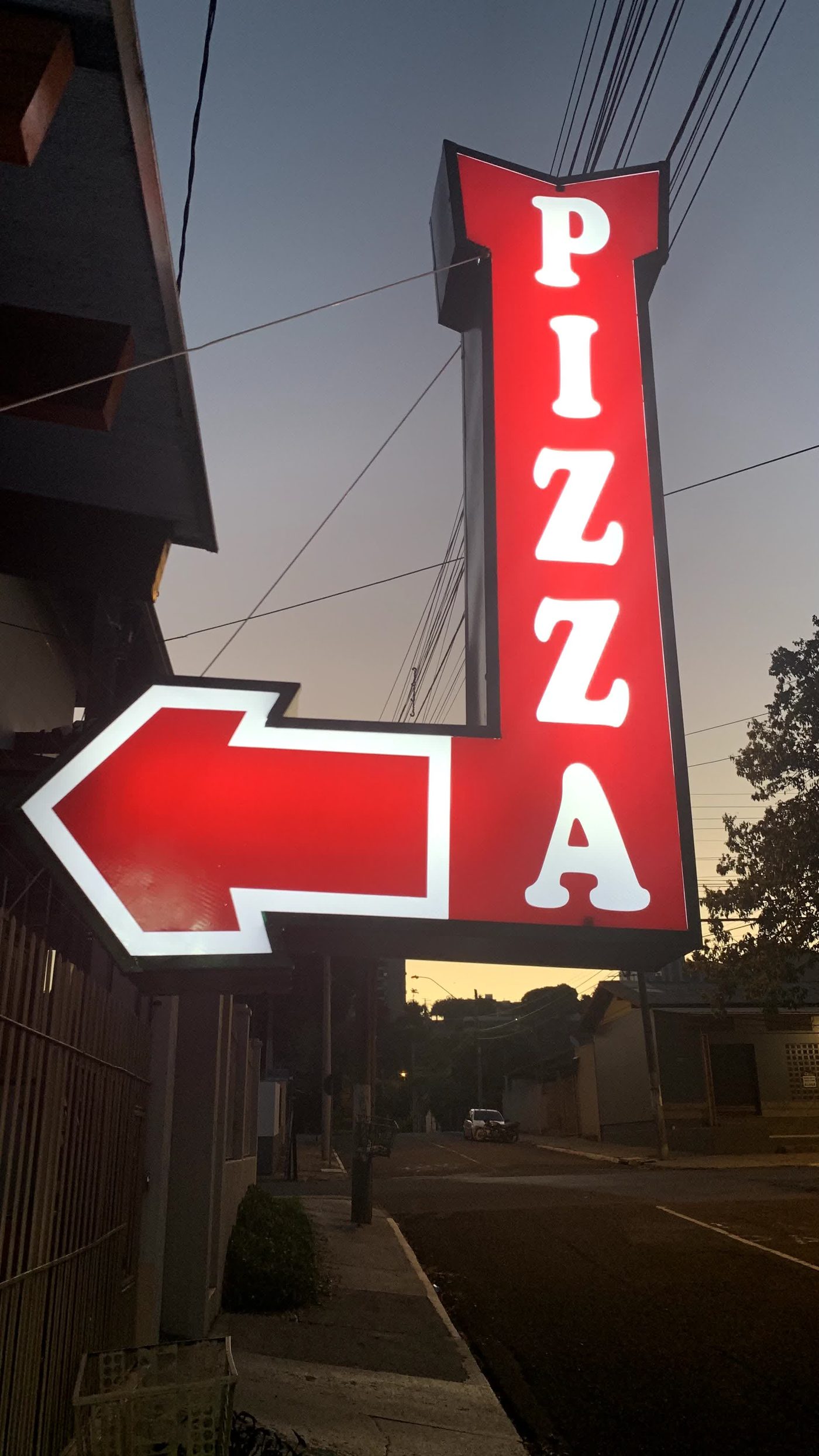 Placa de neon PIZZA da antiga Garage85, apontando a entrada ao anoitecer